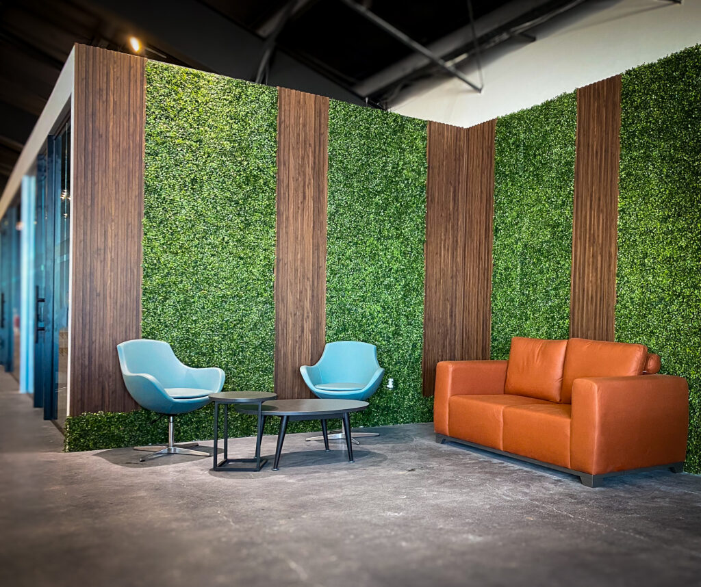 Chic lounge area with a green living wall and wooden panels, featuring a stylish tan sofa and two light blue chairs around a small round table